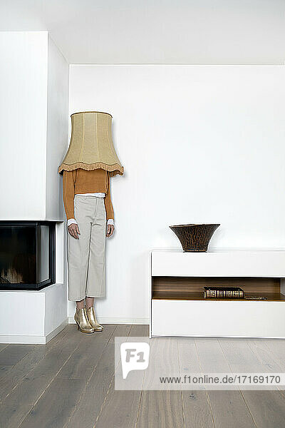 Woman with lamp shade on head standing in corner of wall at home