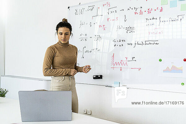 Frau schaut auf Laptop  während sie im Wohnzimmer eine mathematische Formel löst