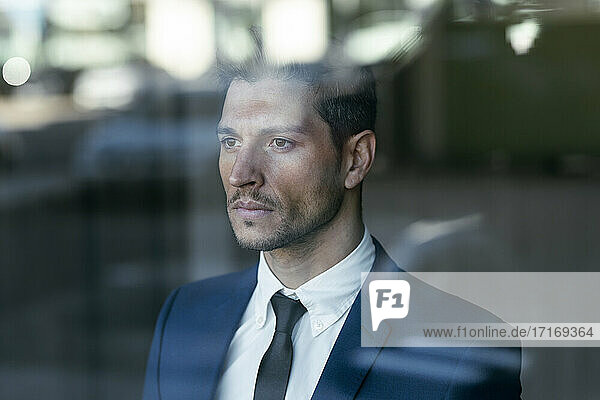 Thoughtful businessman looking through glass window while standing in office