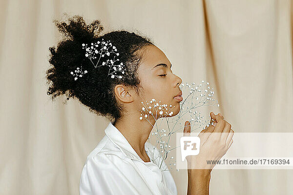 Frau mit geschlossenen Augen riecht an weißen Blumen vor beigem Vorhang