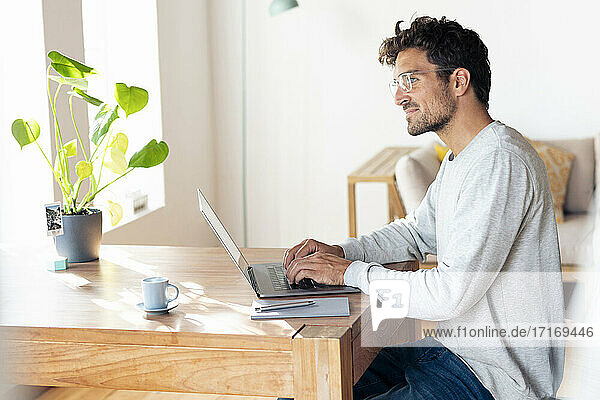 Mann mit Brille  der wegschaut  während er im Büro zu Hause am Laptop sitzt