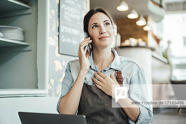 Female owner talking on smart phone while working in cafe