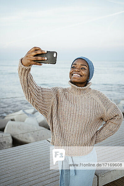 Junge Frau lächelt  während sie ein Selfie mit dem Handy macht und gegen den Himmel steht