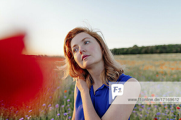 Beautiful woman with hand on shoulder day dreaming in poppy field