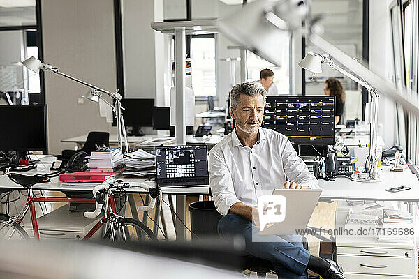 Geschäftsmann  der ein digitales Tablet benutzt  während er mit Kollegen im Hintergrund in einem Großraumbüro sitzt