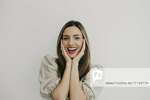 Surprised woman with hand on chin smiling against white background