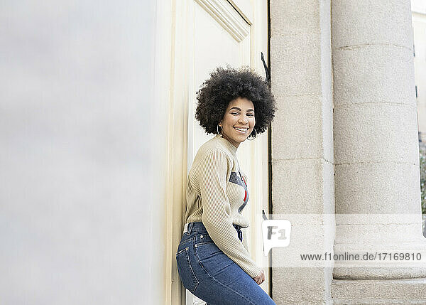 Afro woman smiling while leaning on wall