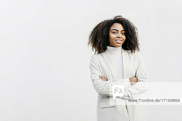 Smiling afro young woman with arms crossed standing against white wall