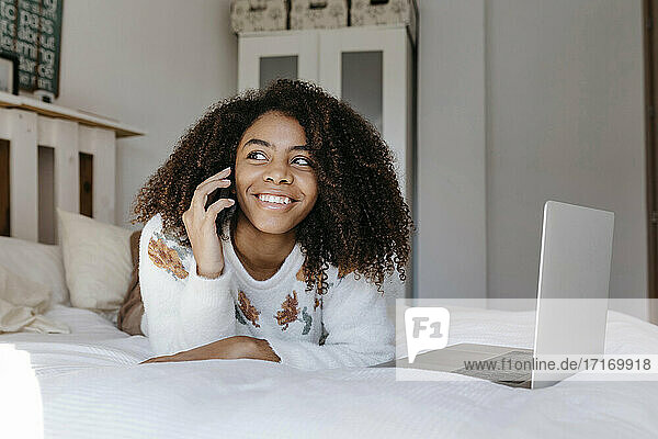 Glückliche Frau  die mit ihrem Handy telefoniert  während sie sich zu Hause auf dem Bett ausruht