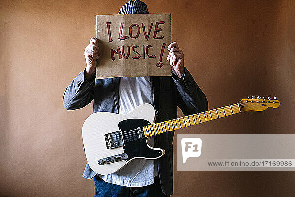 Mature male guitarist holding paper with text against wall