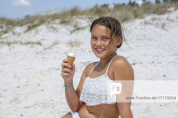 Mädchen lächelnd beim Eis essen am Strand sitzend an einem sonnigen Tag