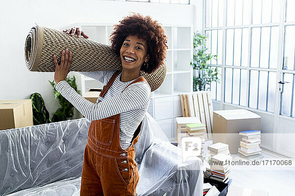 Glückliche Afro-Frau trägt Teppich beim Umzug in ein neues Haus