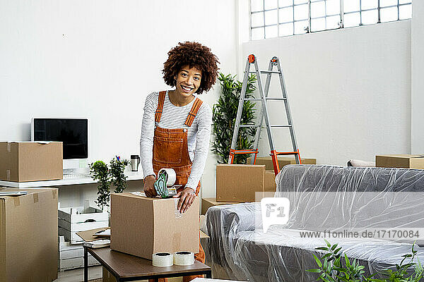 Glückliche junge Frau packt Karton beim Umzug in eine neue Wohnung