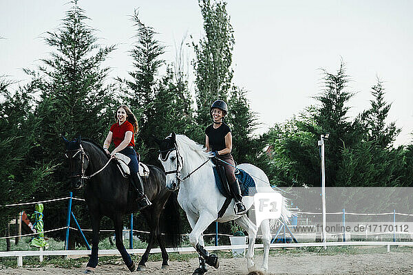 Glückliche Freundinnen reiten auf Pferden in einem Bauernhof