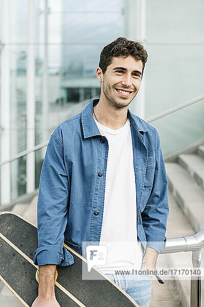 Portrait of smiling young man with skateboard outdoors