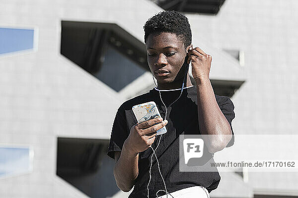 Young man using smart phone while listening music during sunny day