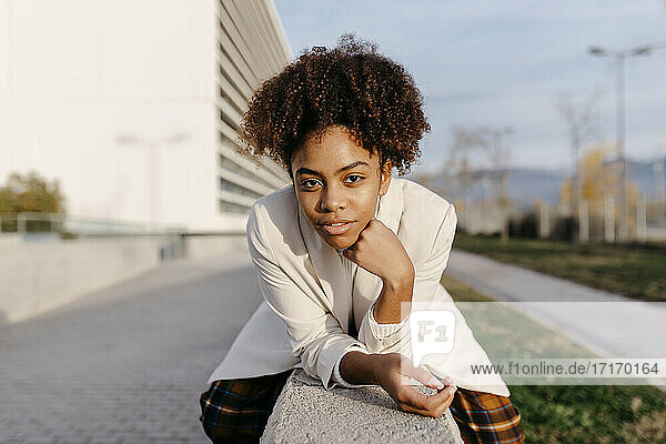 Selbstbewusste junge Frau mit Afro-Haar sitzt auf einer Stützmauer in der Stadt