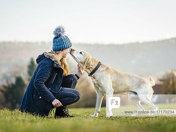 Young woman in knit hat playing with dog in field