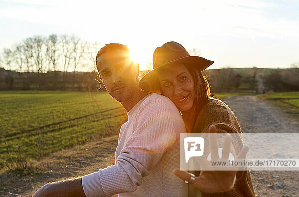 Woman showing Stop gesture while embracing boyfriend from behind during sunset
