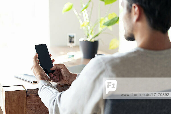 Man checking his mobile phone while sitting on chair at home
