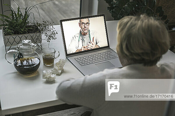 Ein männlicher Arzt berät einen älteren Patienten per Videoanruf auf einem Laptop zu Hause