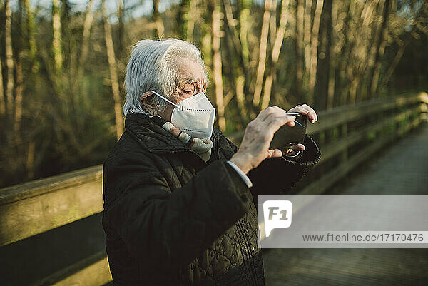 Ältere Frau fotografiert mit ihrem Smartphone auf einer Fußgängerbrücke während COVID-19