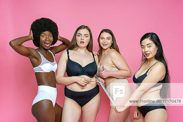 Überrascht Gruppe von multiethnischen weiblichen Modell in Dessous mit Maßband gegen rosa Hintergrund