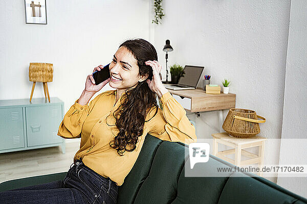 Woman talking on mobile phone while sitting on sofa at home