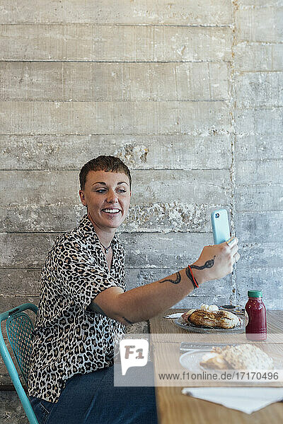 Smiling woman taking selfie through mobile phone while sitting at restaurant