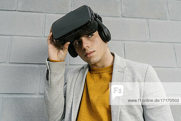 Man removing virtual reality headset while standing against gray wall
