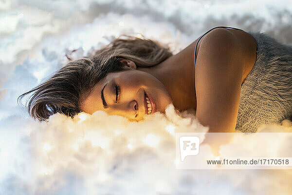 Lächelnde junge Frau  die auf beleuchteten Baumwolltüchern schläft