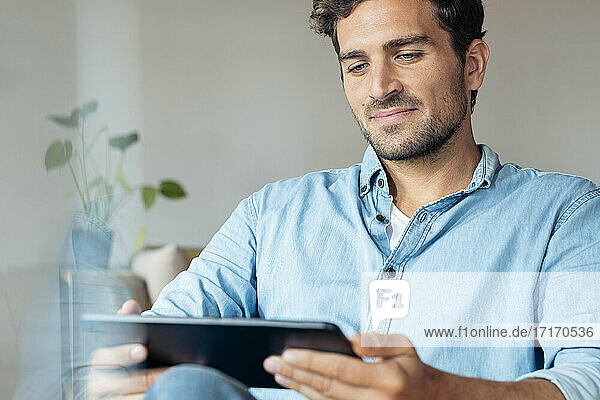 Mann benutzt digitales Tablet  während er zu Hause sitzt