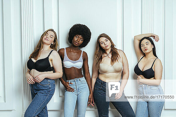 Multi-ethnische Gruppe weiblicher Modelle  die BHs und Jeans tragen und gegen eine Wand posieren