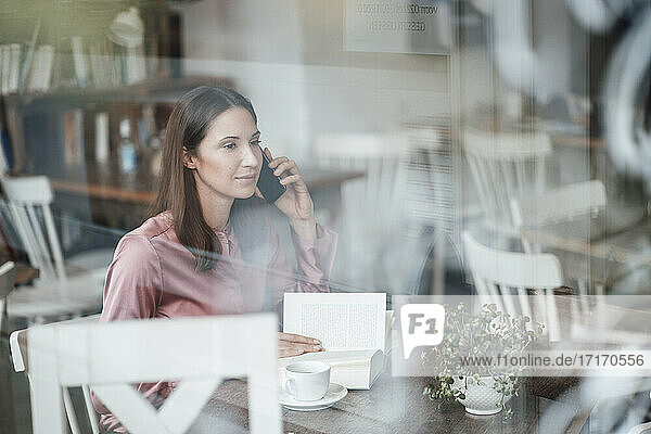 Weibliche Fachkraft mit Buch beim Telefonieren durch Glas im Café gesehen
