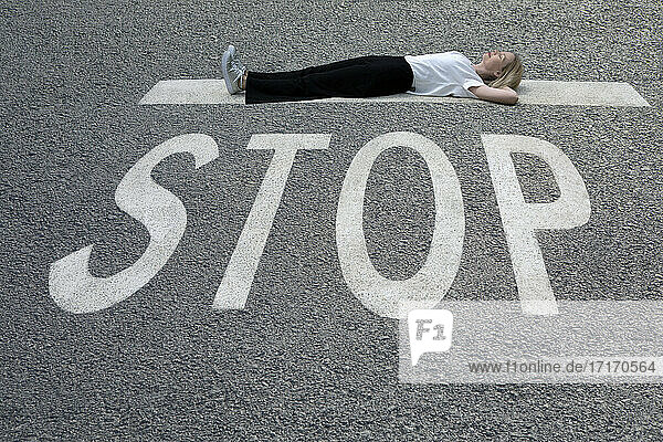 Woman with hands behind head lying down on road at STOP sign