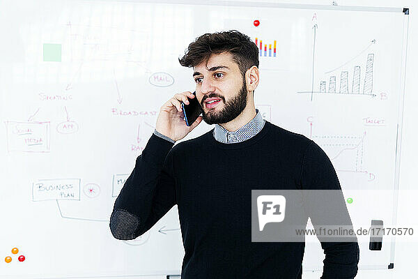 Businessman talking on phone in front of whiteboard in office