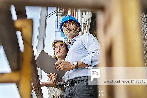 Male architect holding digital tablet while examining construction site with colleague