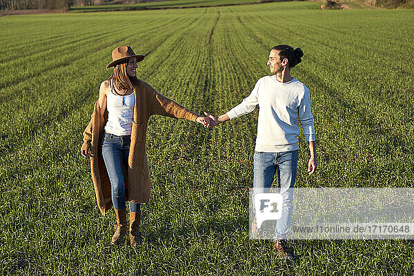 Heterosexual couple with holding hands looking at each other while walking on green land