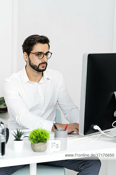 Junger Geschäftsmann mit Brille arbeitet am Computer im Büro