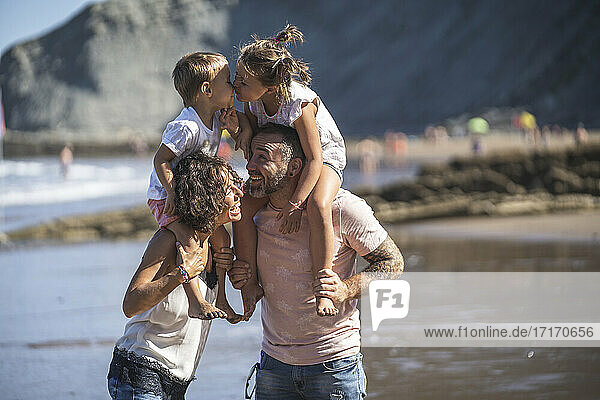 Sibling kissing while sitting on parents shoulder at beach