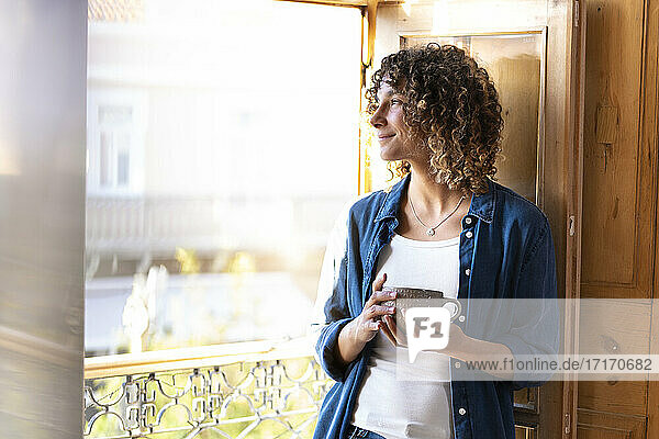 Smiling thoughtful woman with coffee cup looking out of window
