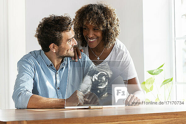 Couple smiling while checking ultrasound image over transparent screen at home