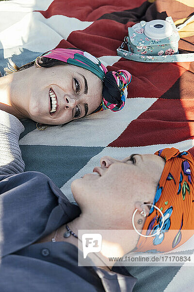 Smiling friends wearing headscarf lying while resting on blanket