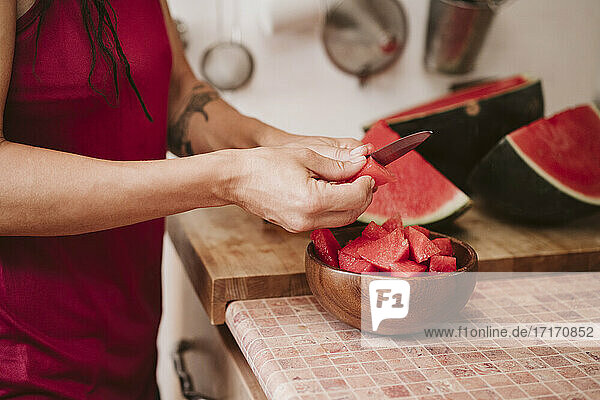 Frau schneidet Wassermelone  während sie in der Küche zu Hause steht