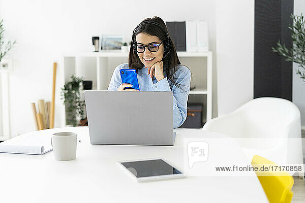 Smiling businesswoman using mobile phone while sitting at office