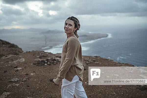 Young woman smiling while walking on mountain against Famara Beach  Lanzarote  Spain