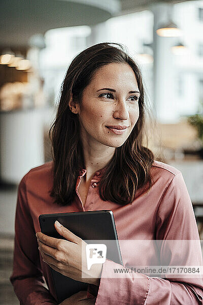 Smiling female professional looking away while holding digital tablet at cafe