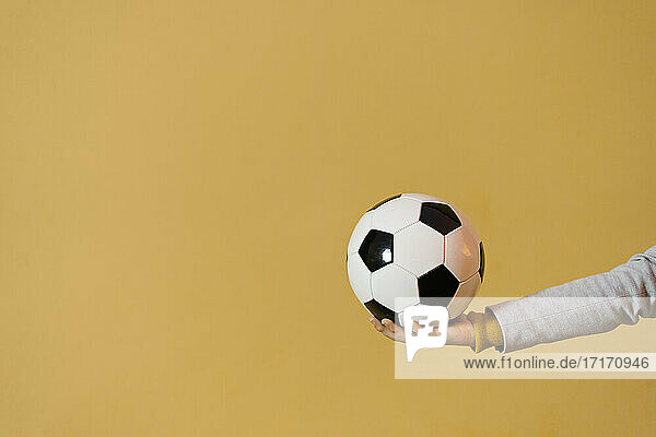 Junger Mann hält Fußball gegen gelbe Wand