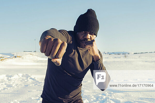Sportsman wearing knit hat practicing while boxing against sky during winter