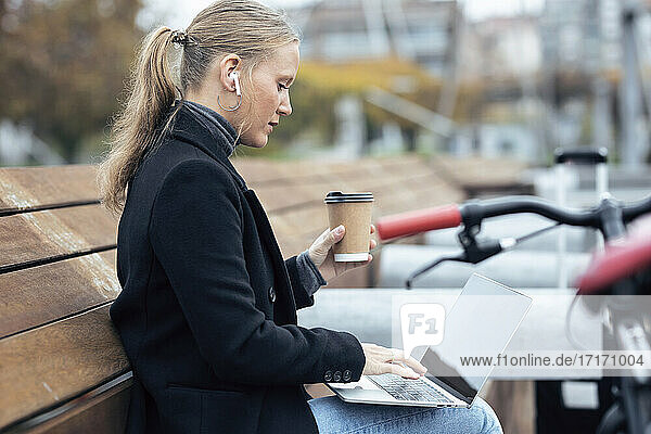 Woman using laptop while holding coffee cup by bicycle